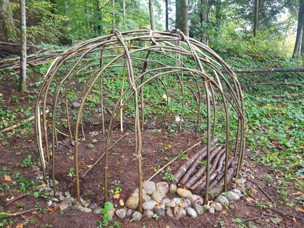 Ein einfaches Häuschen im Wald, nur aus lokalem Material, mit offenem Kamin und einem kleinen Oblicht aus PET-Folie.